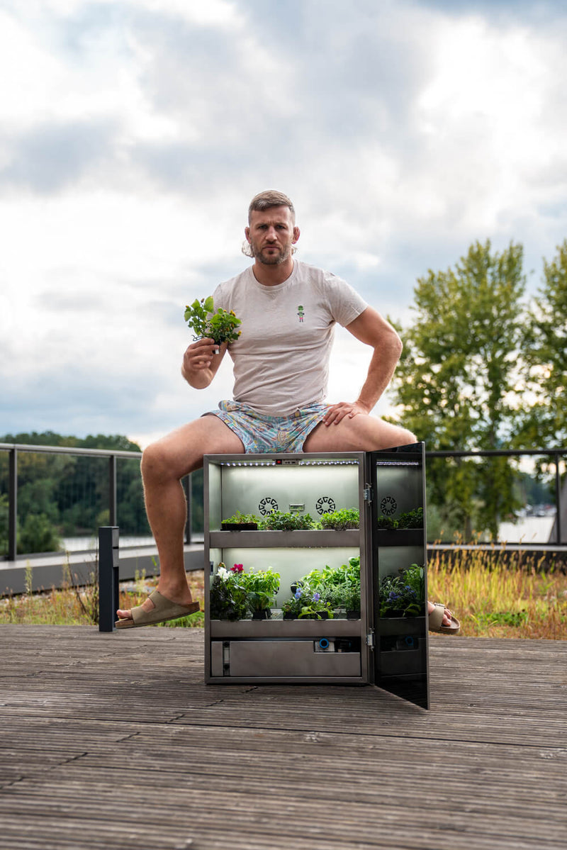Stephan Pütz sitzt auf dem kleinen Raumgarten mit Kräutern in der Hand